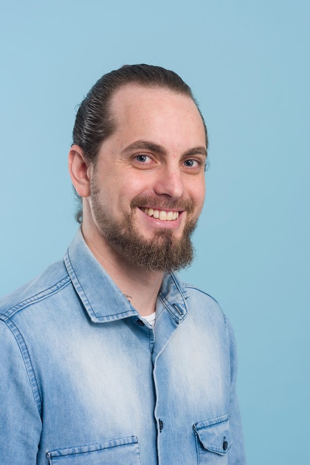 Retrato de Fillipe Rios sorrindo, com camisa azul, diante de um fundo azul-claro